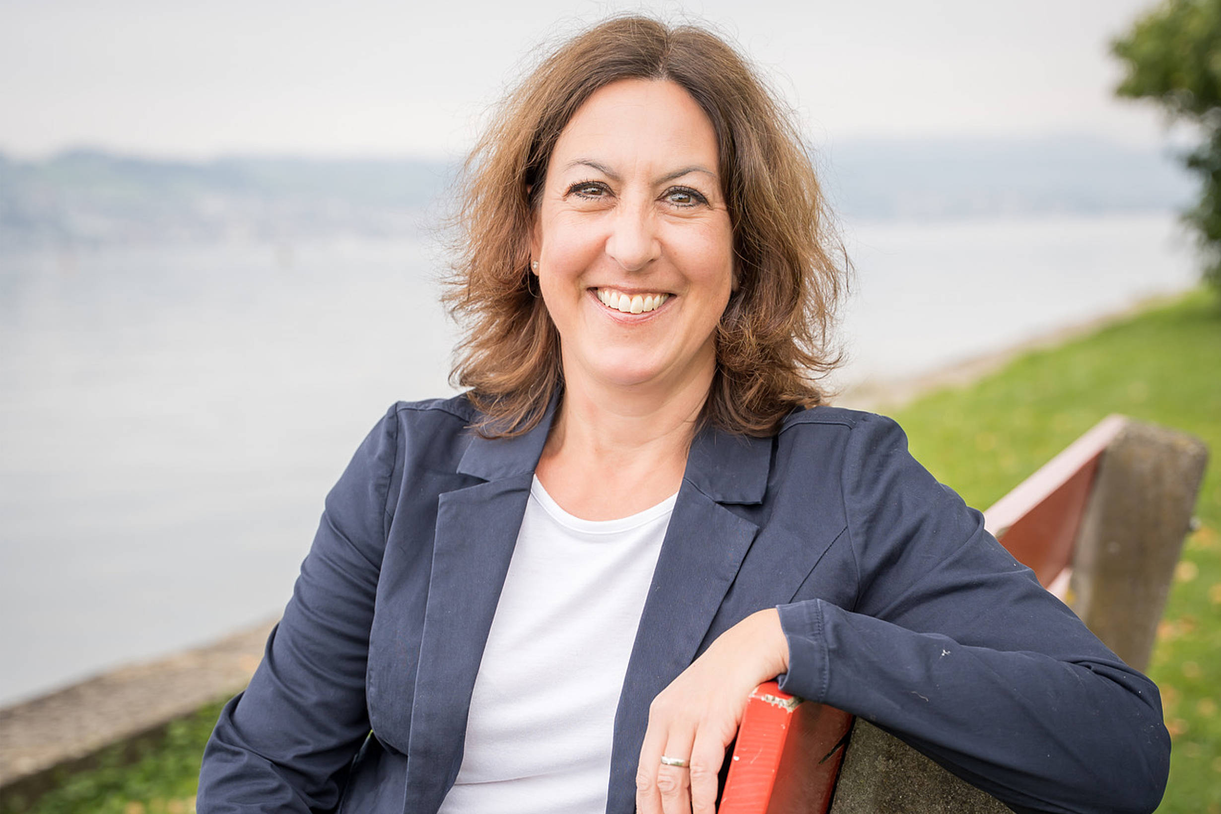 Portrait Karin Birchler Hofbauer Karin Birchler Hofbauer sitzend auf roter Bank am Zürichsee